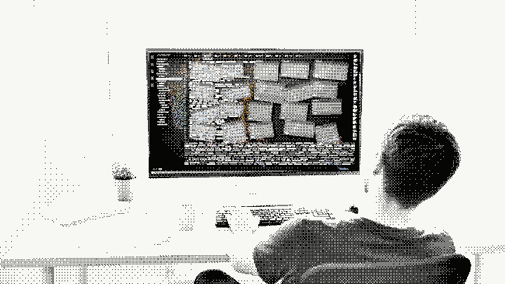 A home office in hard daylight, printed as fine dark dots on paper white, seen over the shoulder of a person hunched at the desk with both hands on the keyboard. The wide monitor facing the camera shows a code editor buried under a dozen overlapping panels, its tab row crammed and its terminal full. A mug, a plant and a slipped stack of papers sit at the left, a bright window behind.